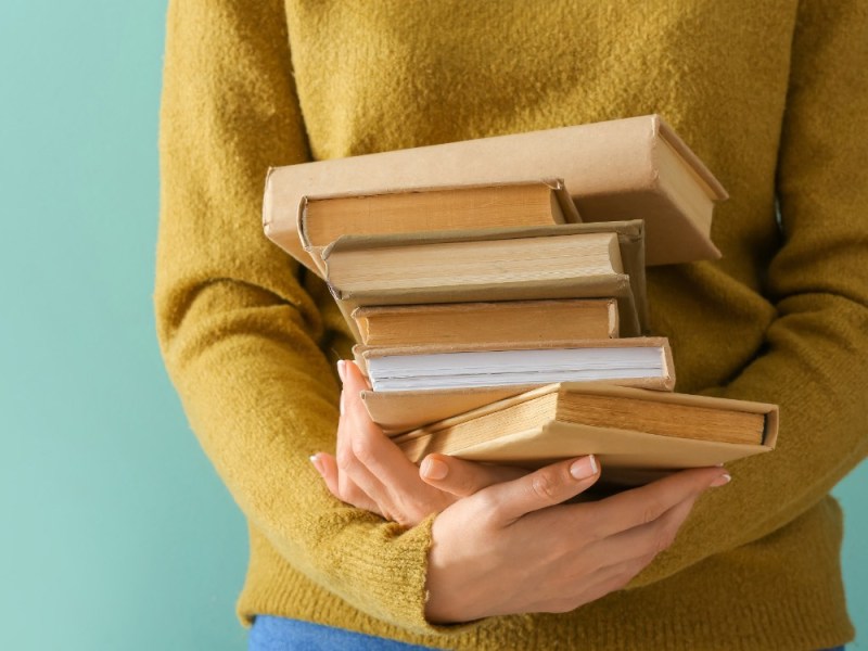 Eine junge Frau hält einen Stapel Bücher in den Händen.