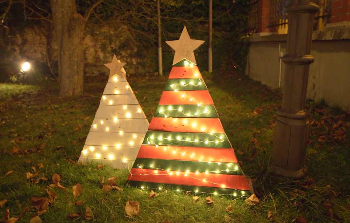 Zwei aus Paletten gebastelte WeihnachtsbÃ¤ume stehen abends in einem Garten, von Lichterketten erleuchtet.