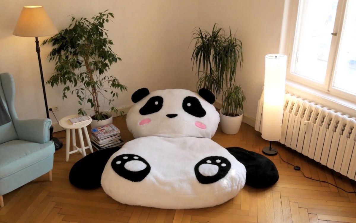 Ein großes Panda-Kuscheltier, das als Kissen benutz werden kann, liegt in einem Wohnzimmer.