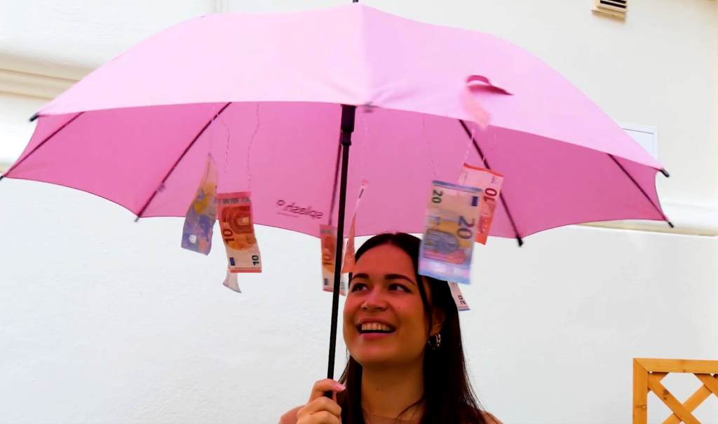 Eine junge Frau hält einen roten Regenschirm, an dem Geldscheine befestigt wurden.