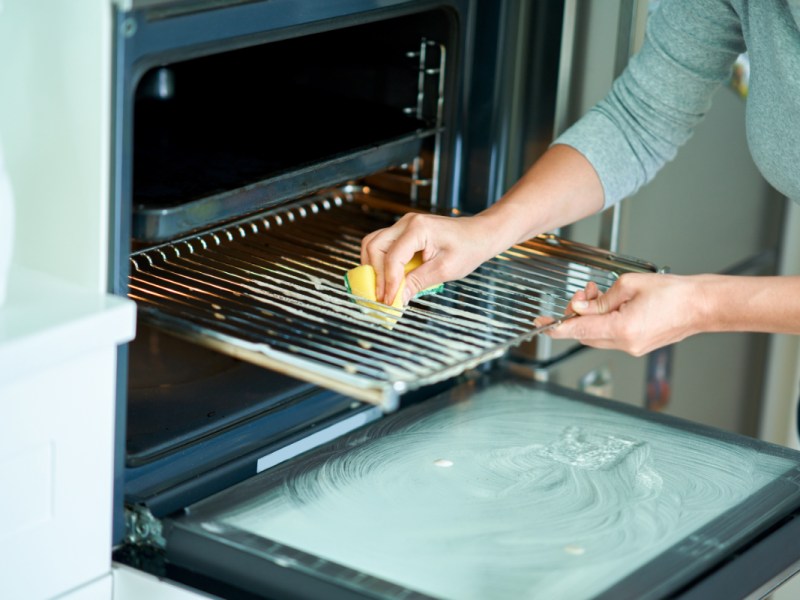 Ein Foto zeigt eine Frau beim Backofen reinigen.