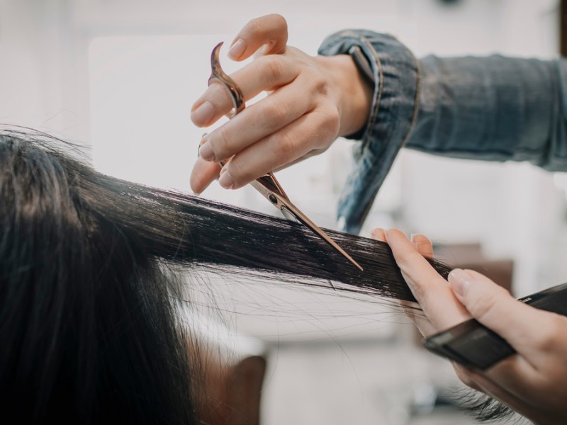 Eine Friseuse schneidet eine Strähne schwarzen Haares einer Kundin.