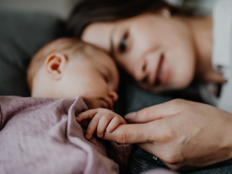 Eine glückliche junge Mutter liegt neben ihrem schlafenden Baby.