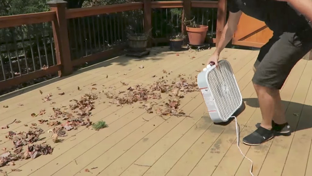 Ein Mann pustet mit einem Ventilator Herbstlaub von seiner Veranda.