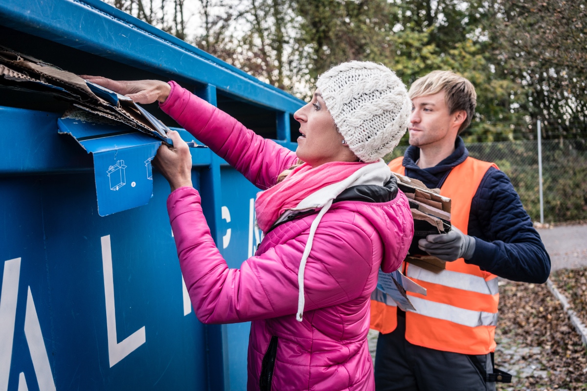 Ein Mann und eine Frau entsorgen Kartons und Pappe in einem Altpapiercontainer.