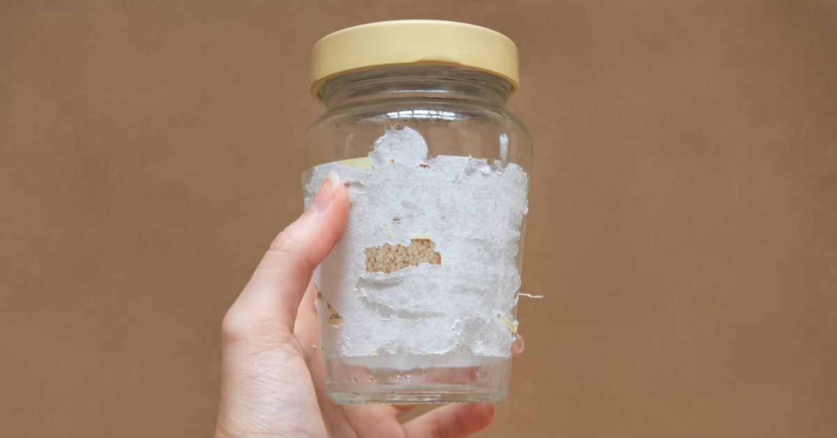 Jemand hält ein Glas in der Hand, bei welchem das Etikett nicht vollständig entfernt werden konnte. Mithilfe des Kriechöls WD-40 kannst du den Aufkleber lösen und restlos entfernen.