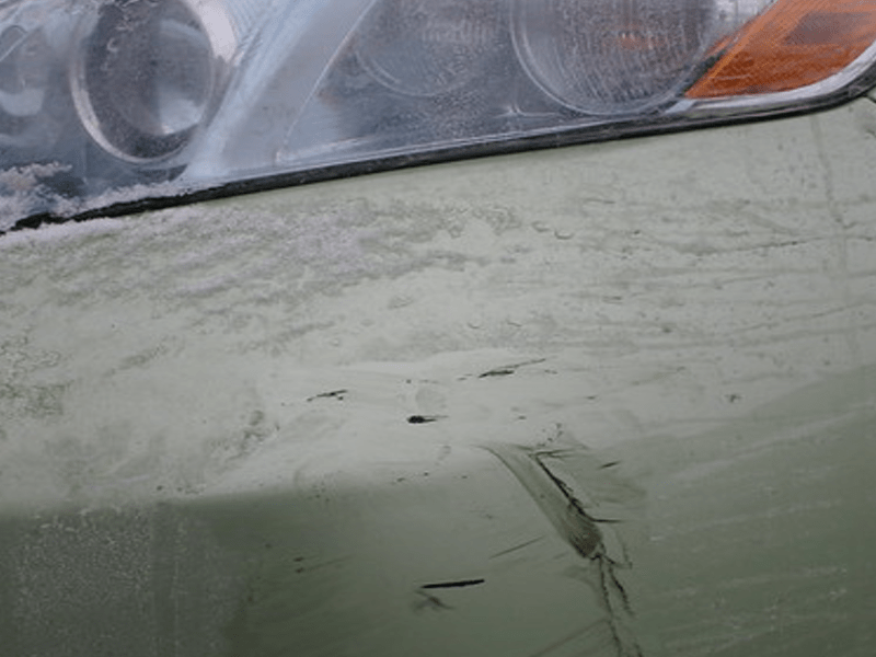Ein Auto, das unterhalb des Scheinwerfers Farbflecken und Lackkratzer aufweist.