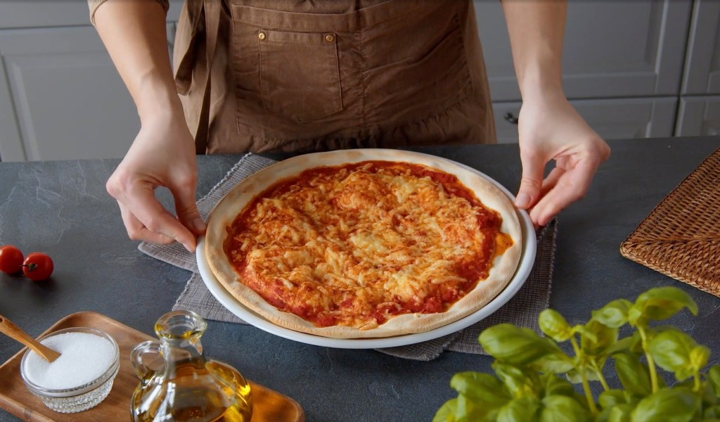 Eine Köchin richtet eine Pizza auf einem Teller an.