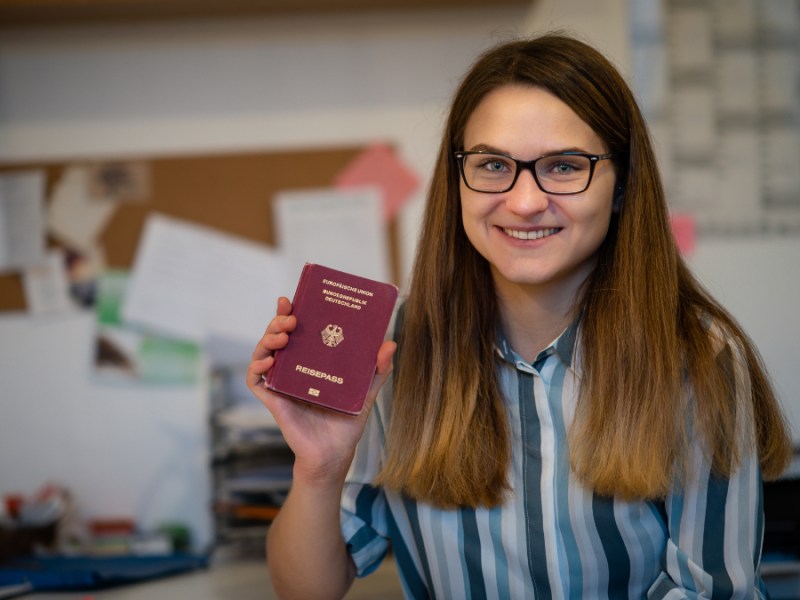 Eine junge Frau hält stolz ihren Reisepass hoch.