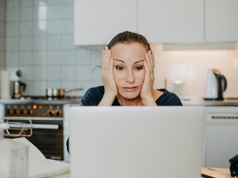 Eine Frau rauft sich die Haare und sitzt vor einem Laptop.