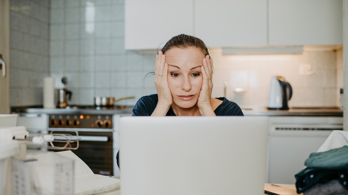 Eine Frau rauft sich die Haare und sitzt vor einem Laptop.