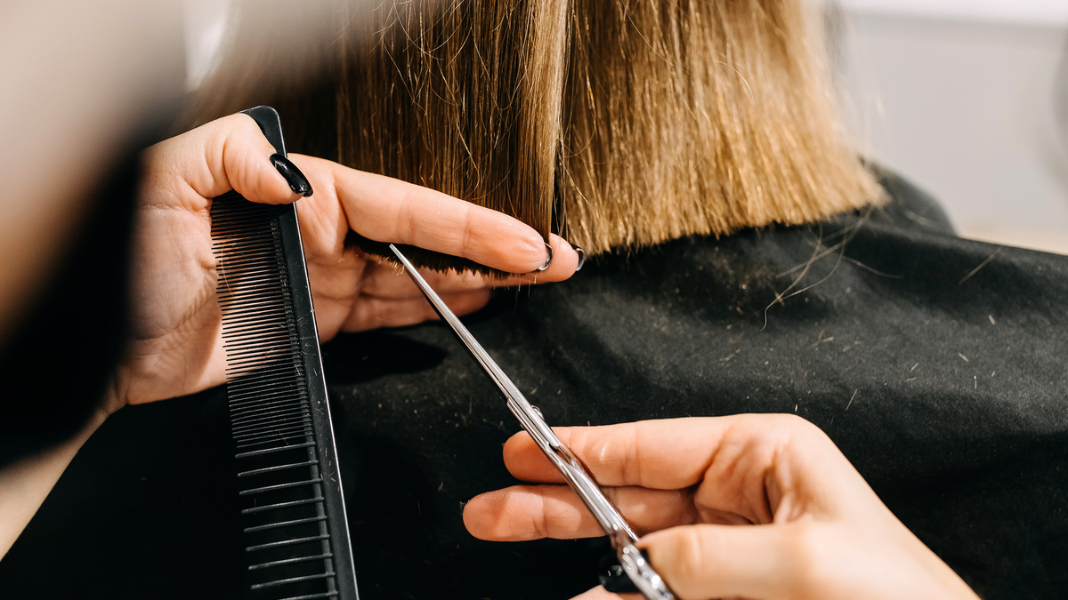 Einer Frau werden die Haare mit Kamm und Schere geschnitten.