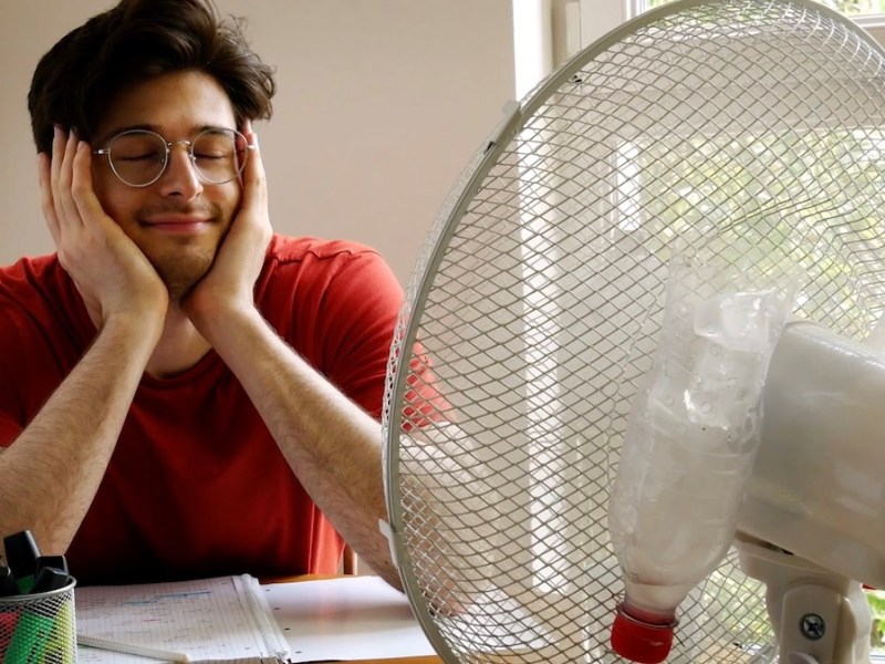 Ein Mann sitzt glücklich vor einem laufen Ventilator.