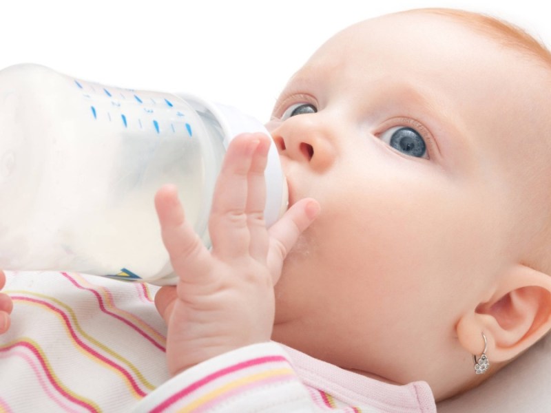 ein Baby mit Ohrringen nuckelt an einer Milchflasche