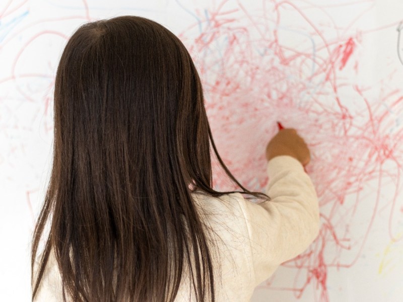 Mädchen malt mit einem roten Stift die Wand an