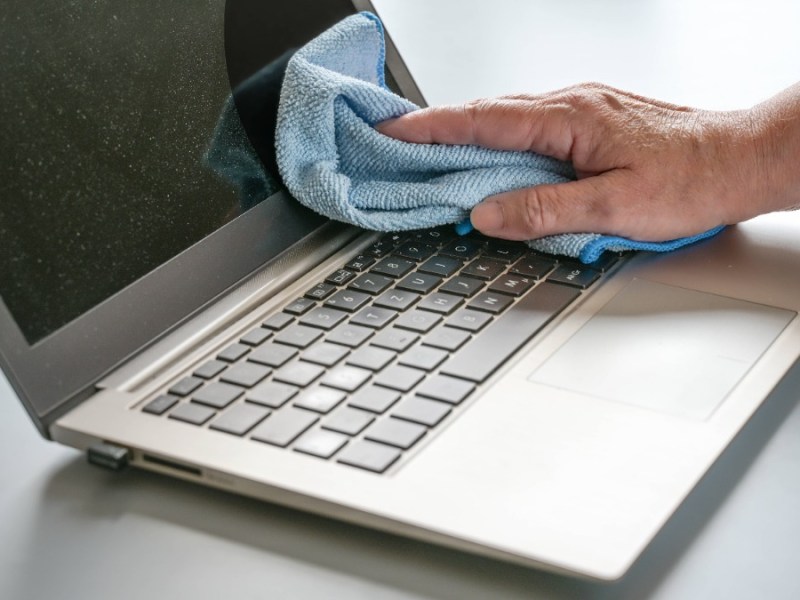 Laptop Bildschirm reinigen: Handreinigung eines verstaubten Laptops mit einem blauen Tuch