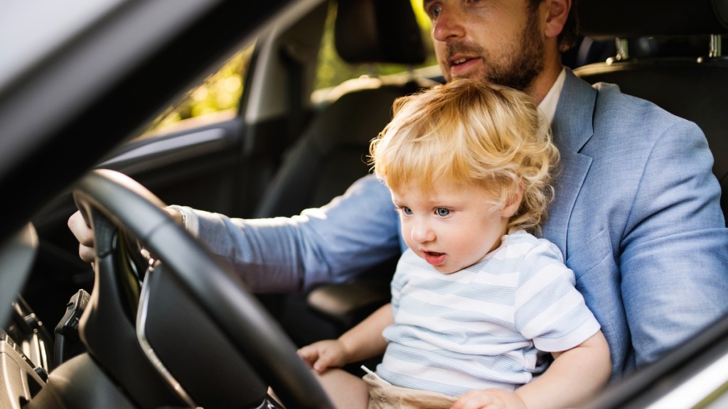 Ein Mann sitzt am Steuer des Autos und hat ein Kleinkind auf dem Schoß.