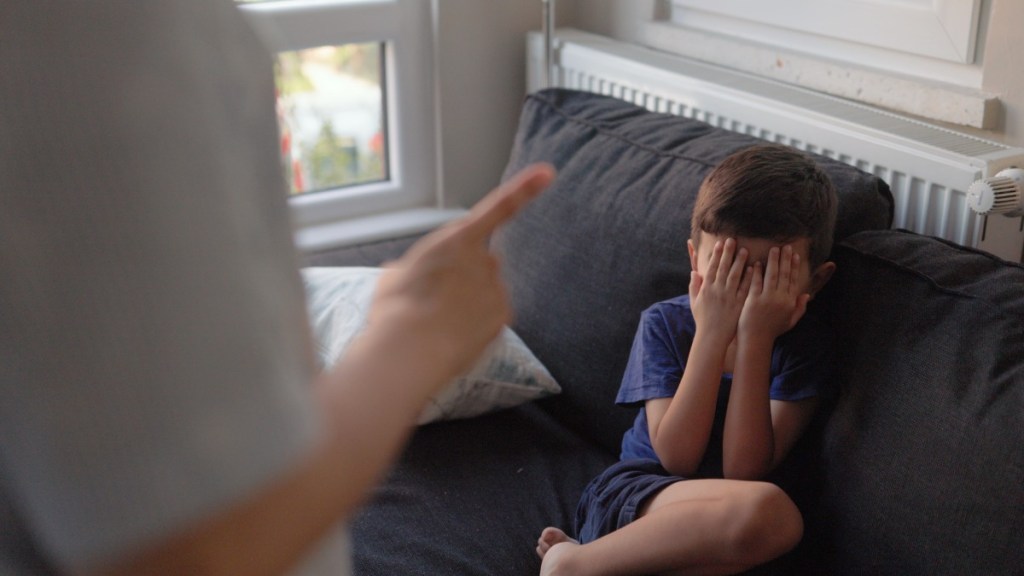 Junge bedeckt seine Augen mit den Händen während der Vater mit ihm schimpft