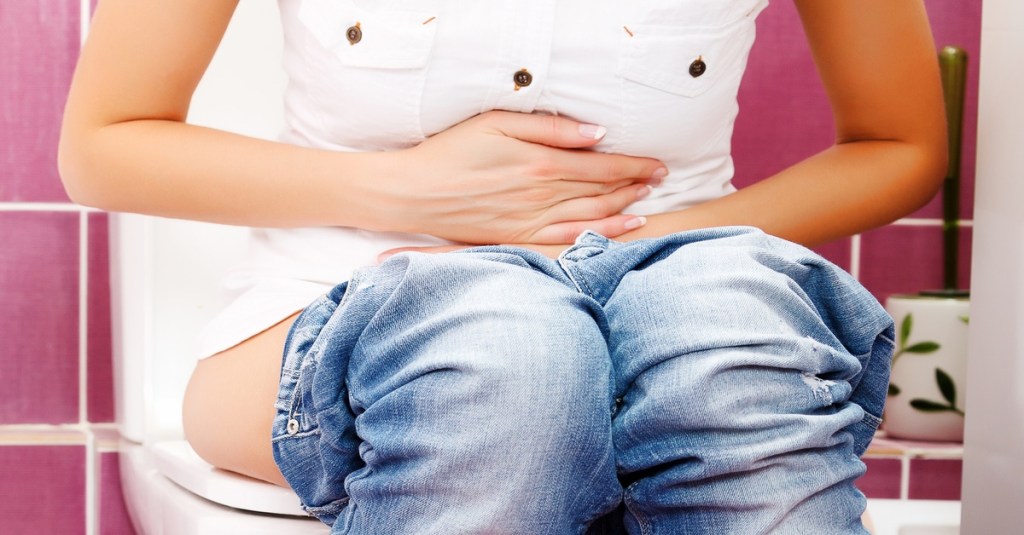 Frau sitzt auf Toilette und hält sich den Bauch.