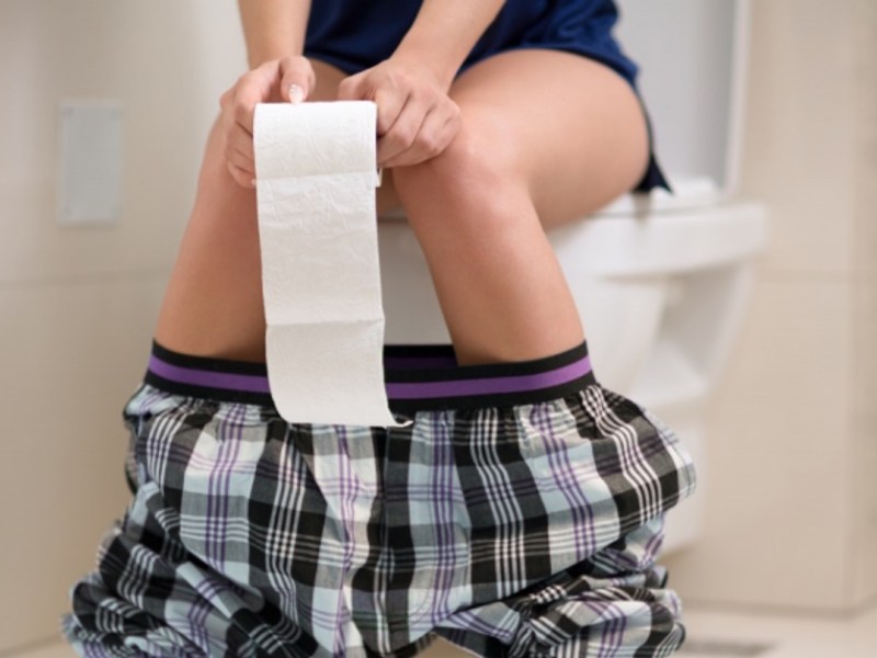 Frau sitzt auf Toilette.