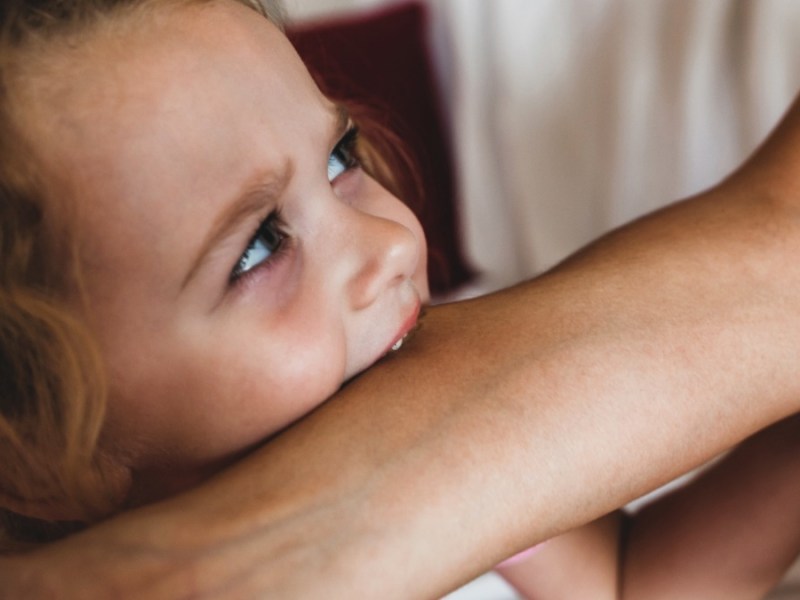 kleines Mädchen beißt Mutter in den Arm