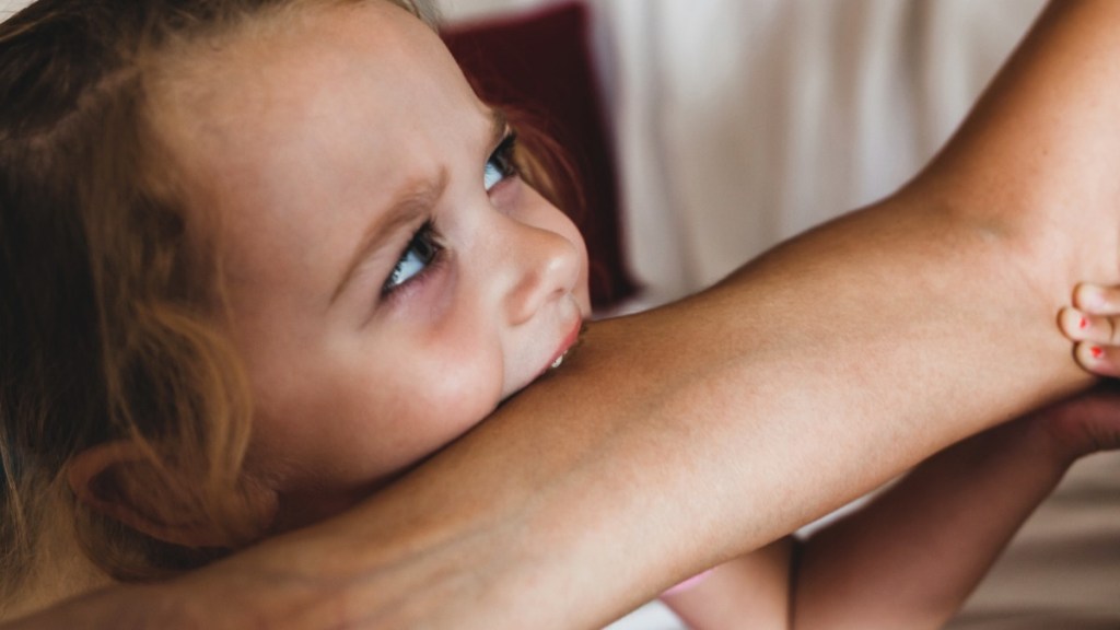 kleines Mädchen beißt Mutter in den Arm