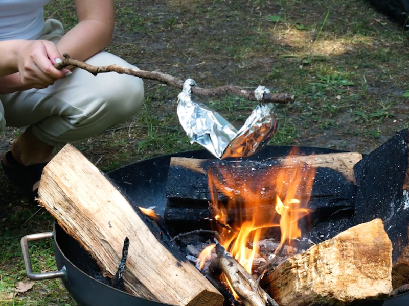 Jemand hält das Alu Päckchen mit Maiskörnern über offenes Feuer, damit Popcorn entsteht