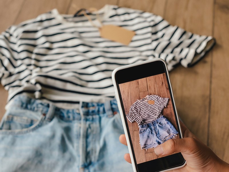 Eine Frau fotografiert mit ihrem Handy ein T-Shirt und eine kurze Hose.