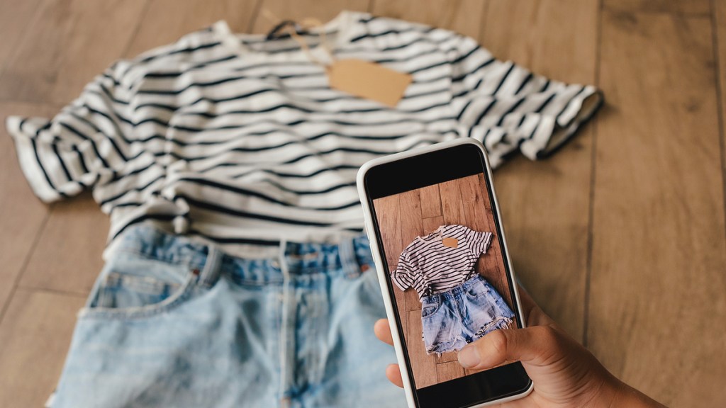 Eine Frau fotografiert mit ihrem Handy ein T-Shirt und eine kurze Hose.