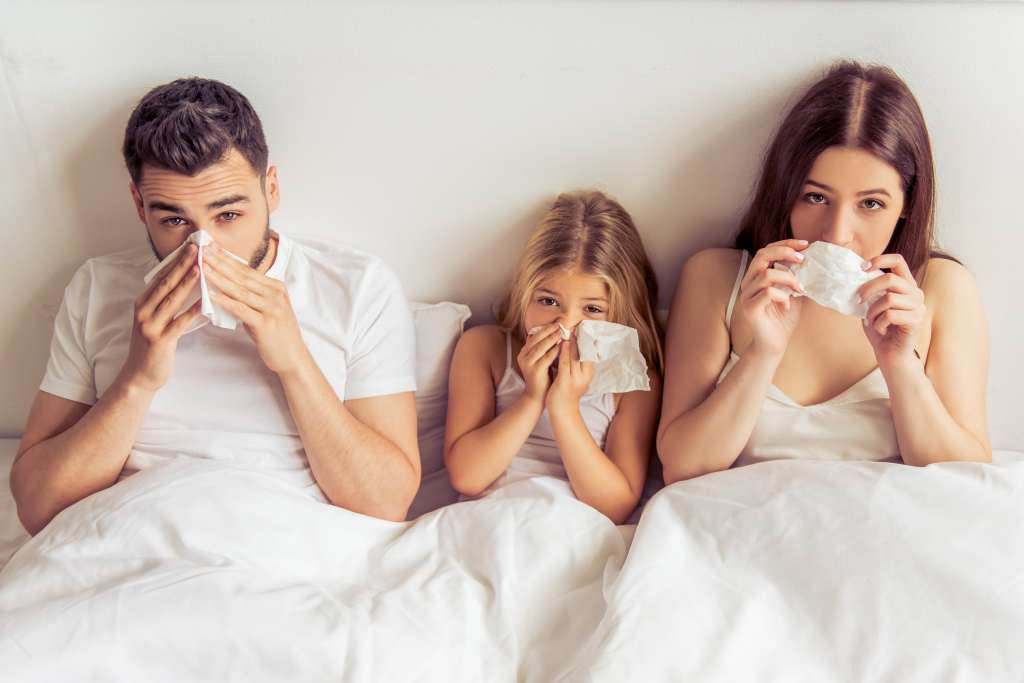 Eine Familie liegt im Bett und ist erkältet.