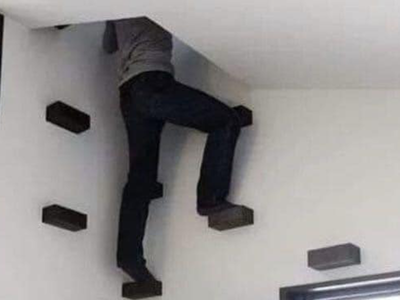 Eine Person klettert mithilfe von schwarzen Trittsteine die Wand durch hinauf, durch ein Einstieg in der Decke