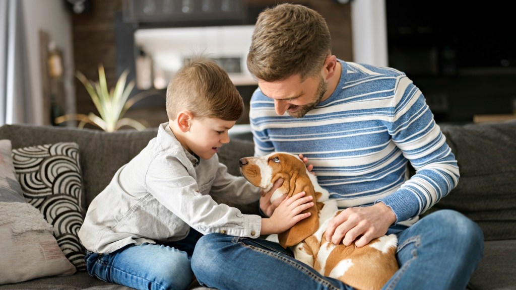 Vater und Sohn streicheln einen Hund auf der Couch.