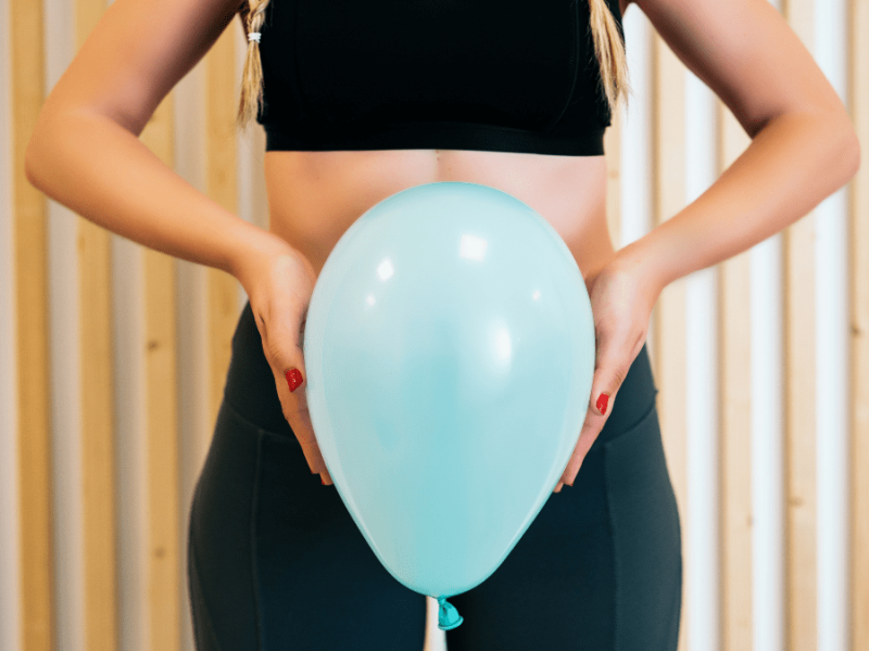 Eine Frau steht mit einem Luftballon vor dem Bauch vor einer Wand.