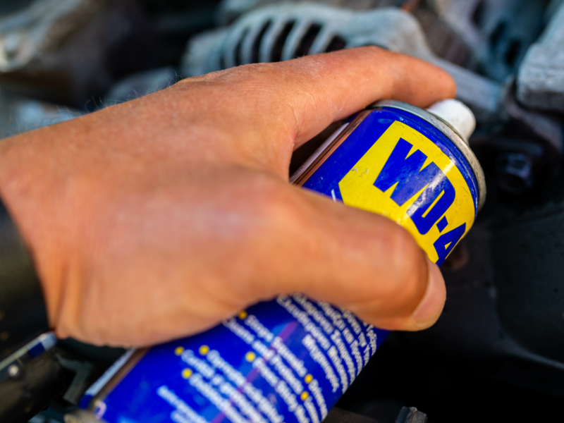 Eine Hand hält eine Dose WD-40 über eine verrostete Stelle