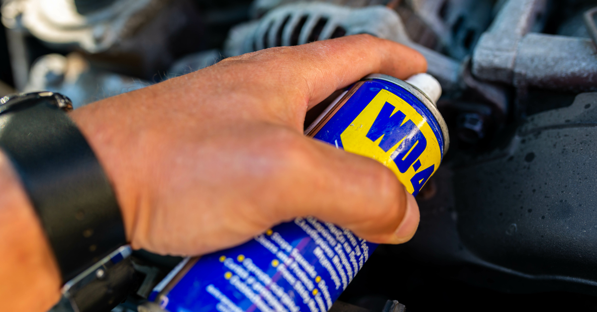 Eine Hand hält eine Dose WD-40 über eine verrostete Stelle