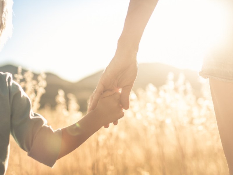 Mutter und Kind halten sich an der Hand und gehen über ein Feld