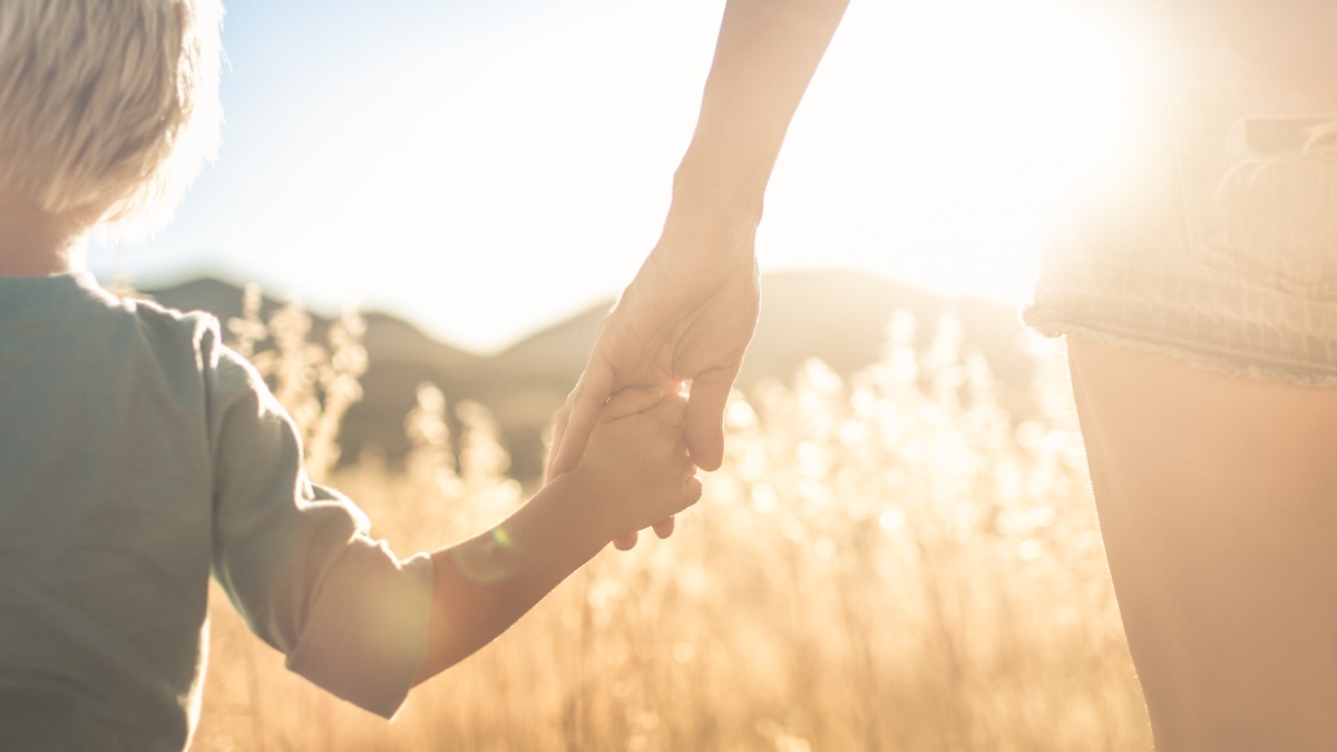 Mutter und Kind halten sich an der Hand und gehen Ã¼ber ein Feld