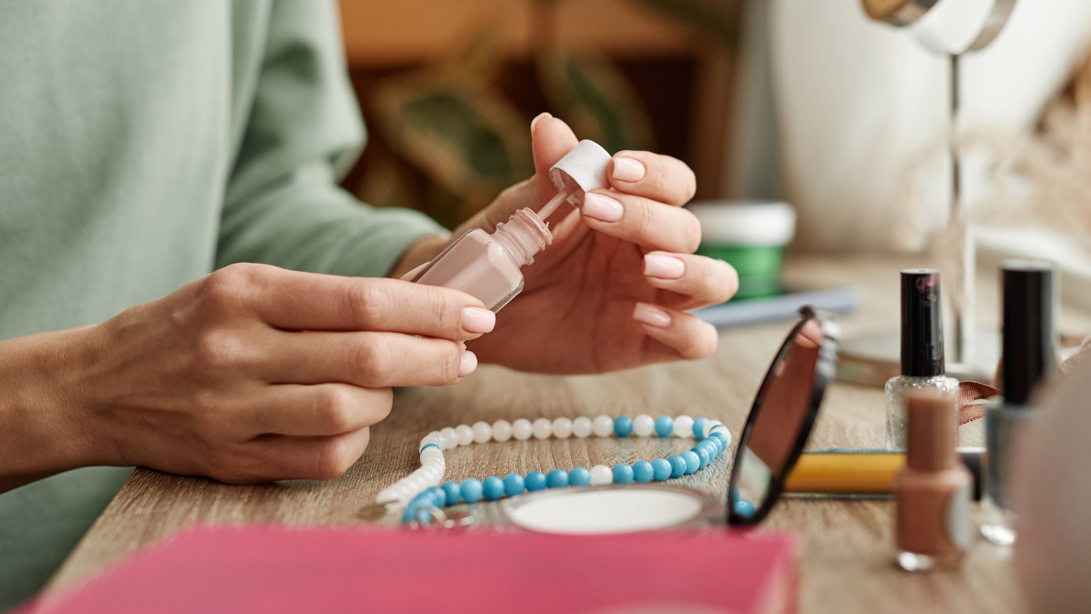 Eine Frau lackiert ihre Fingernägel mit hellem Nagellack.