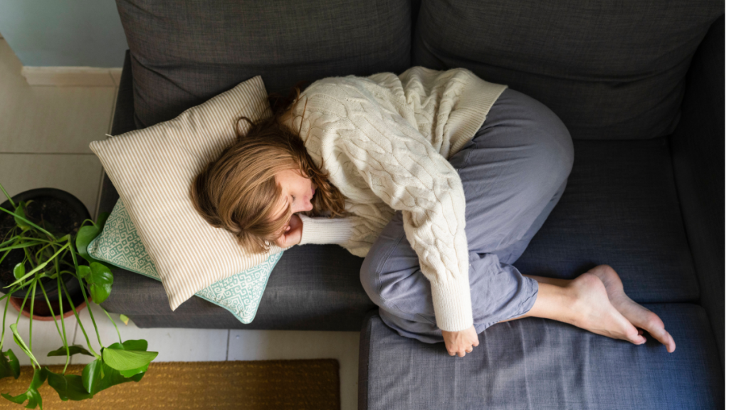 Eine Frau liegt in Embryonalstellung auf einer Couch.