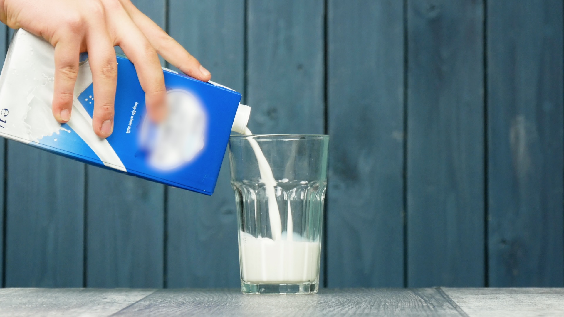 Milch wird aus einem Tetrapak in ein Glas eingeschenkt.