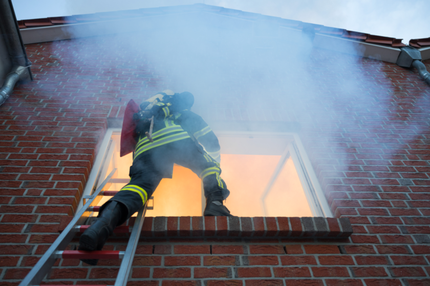 Feuerwehrmann auf einer Leiter, der ein Feuer in einer Wohnung löschen will.