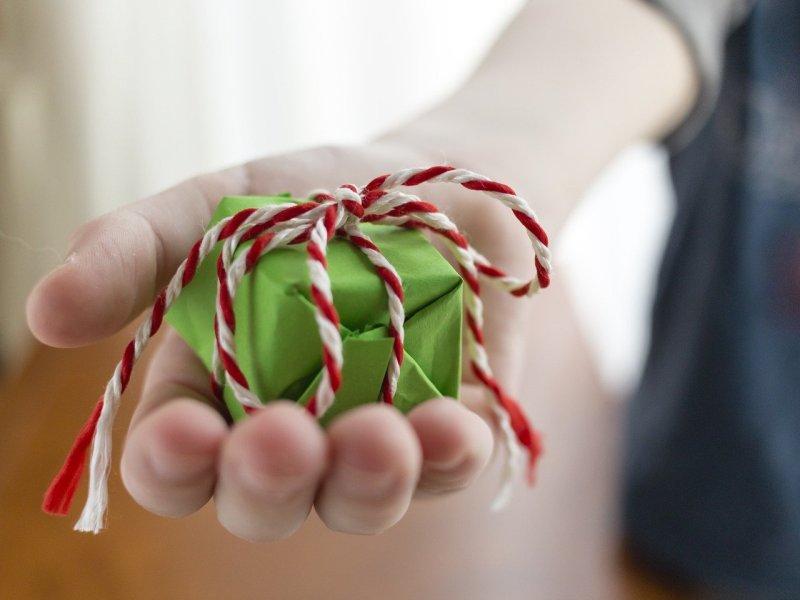 Eine Frau hÃ¤lt ein kleines, grÃ¼nes Geschenk mit Schleife in der Hand.