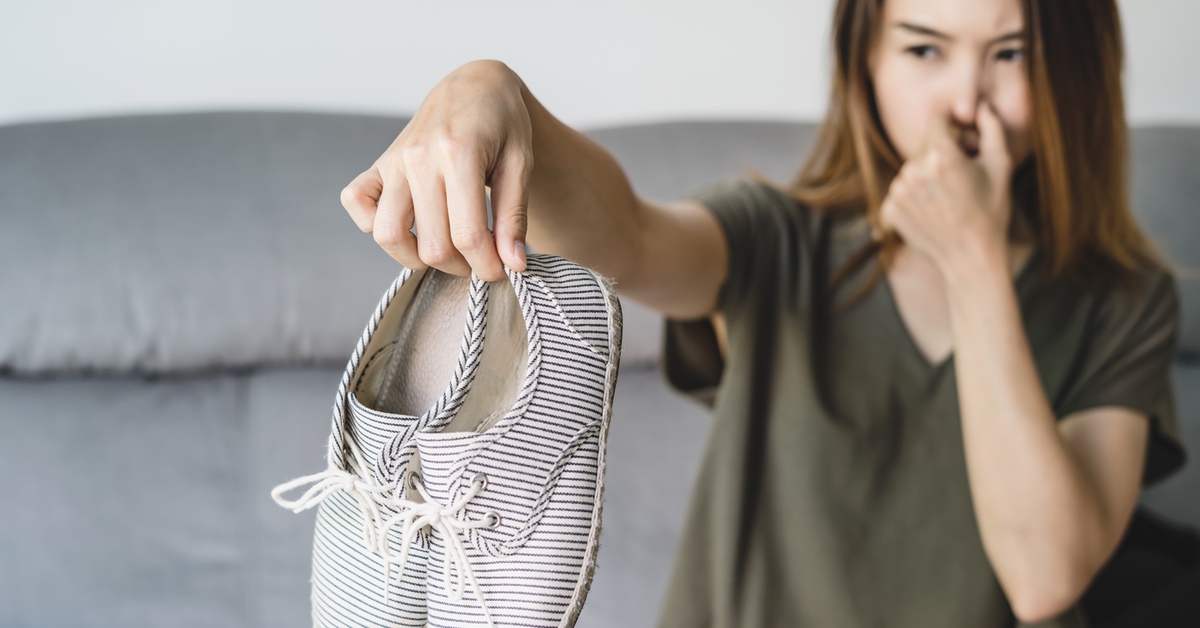 Eine Frau mit braunen Haaren hÃ¤lt helle gestreifte Schuhe hoch und hÃ¤lt sich die Nase zu.