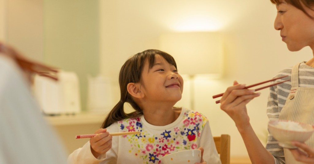 Mutter und Tochter essen gemeinsam und lächeln sich an