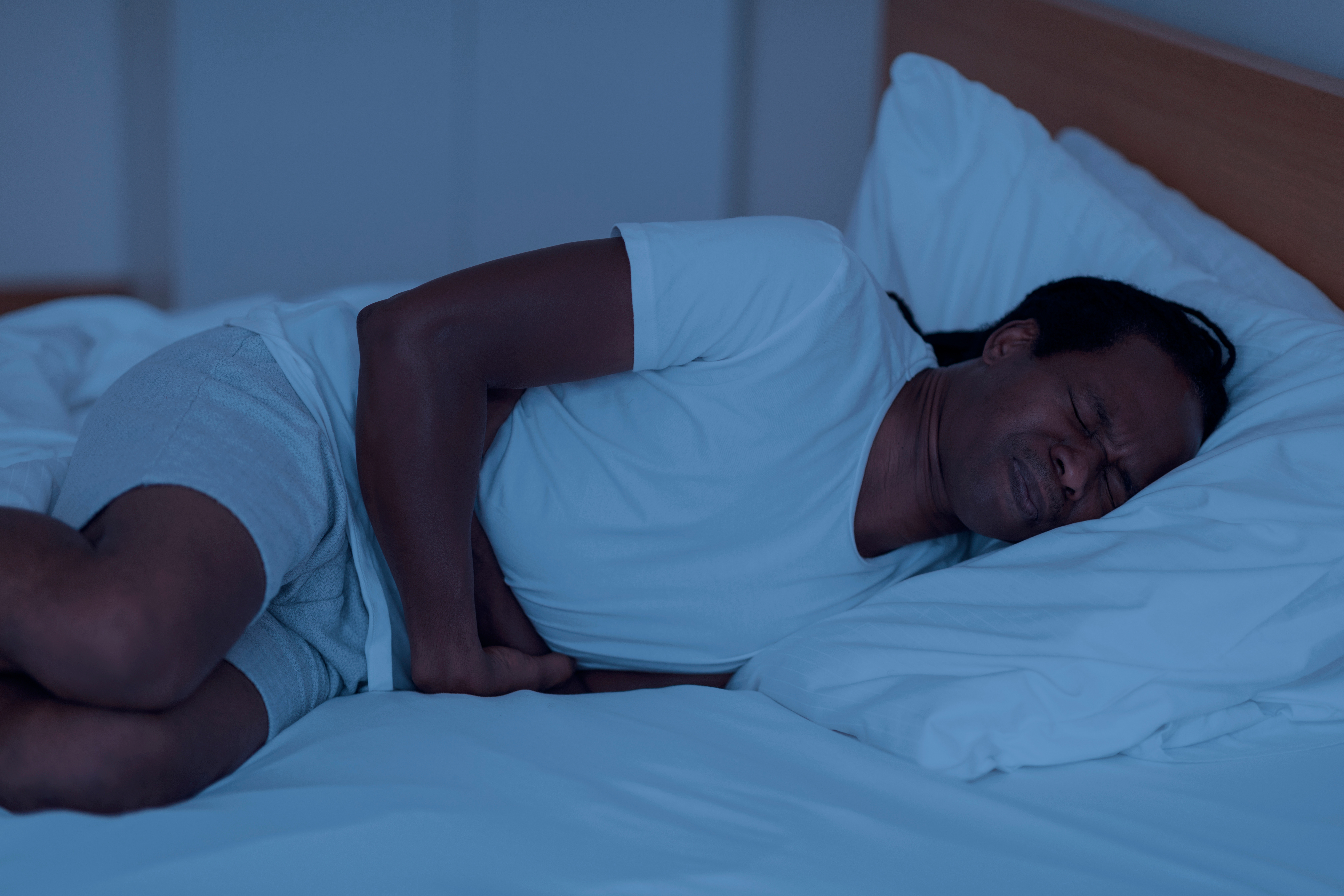 Ein Mann liegt in seinem Bett und krümmt sich vor Schmerzen.