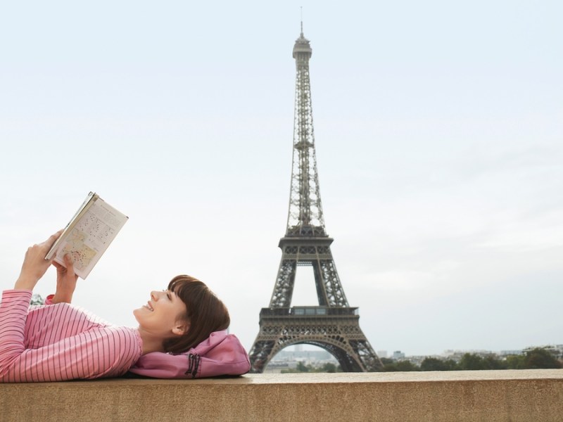 Frau liest ein Buch in Paris – im Hintergrund der Eiffelturm.