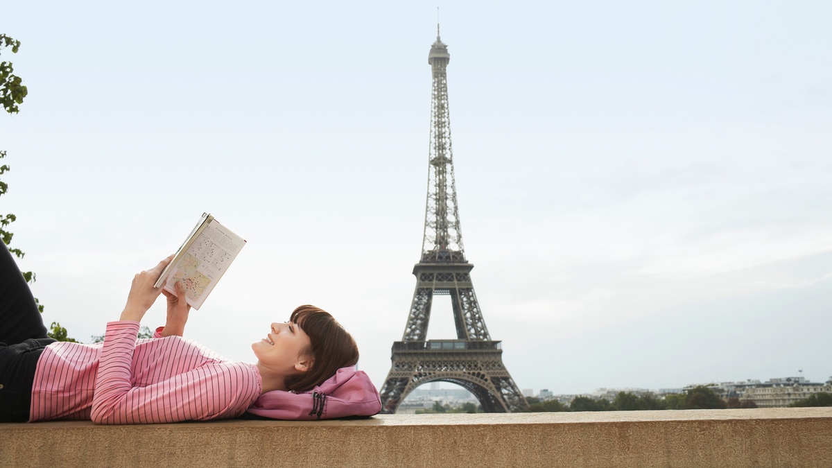 Frau liest ein Buch in Paris â€“ im Hintergrund der Eiffelturm.