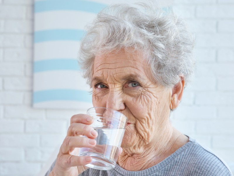 Alte Frau trinkt ein Glas Wasser.