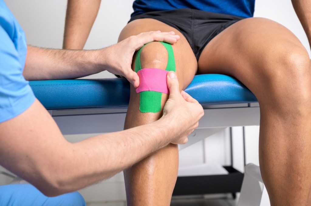 Ein Physiotherapeut behandelt das Bein eines Patienten mit Kinesio-Tape.