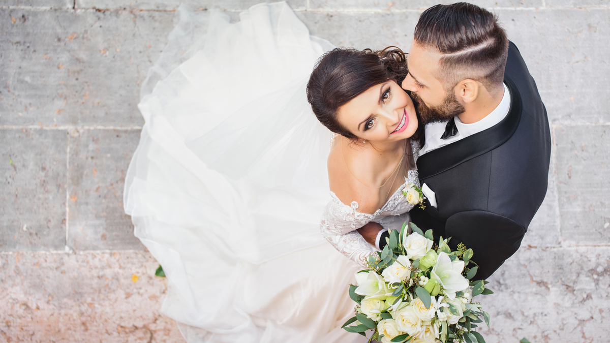 Ein Hochzeitspaar wird von oben fotografiert. Die Braut schaut glÃ¼cklich nach oben in die Kamera.